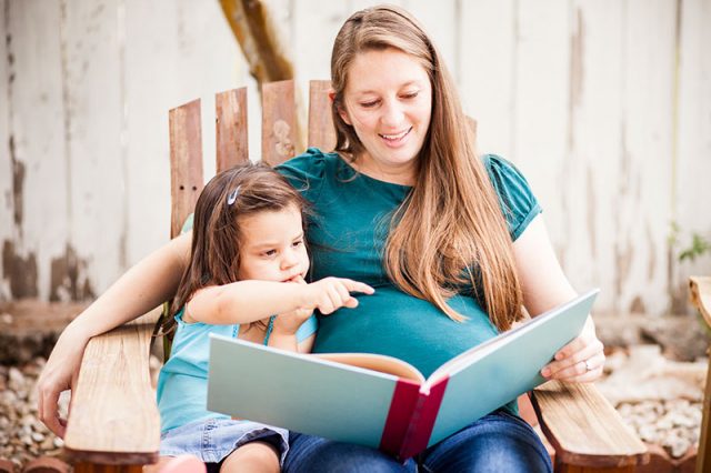 Pregnant mom sits with her young daughter reading a book. CDC says pregnant woman are more susceptible to the coronavirus, there is no evidence that children are.